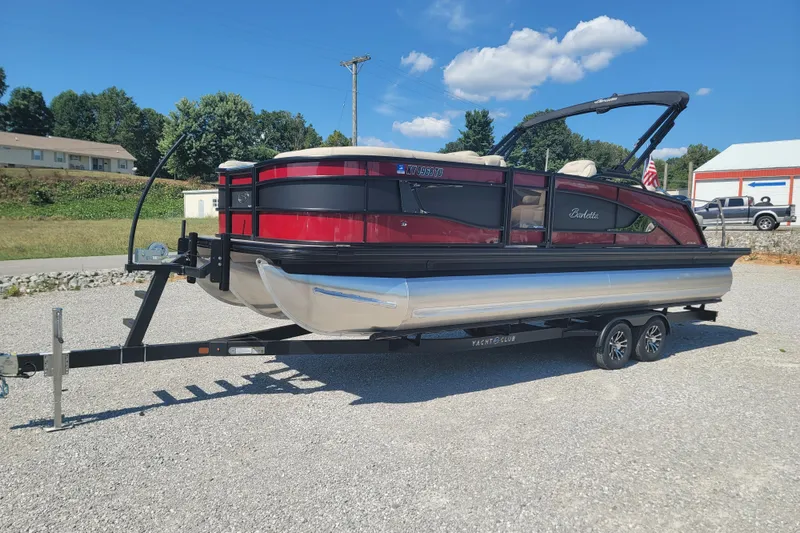 Slide: The Image of 2022 Barletta L23UC pontoon boat on trailer, red and black design, parked outdoors. - 1