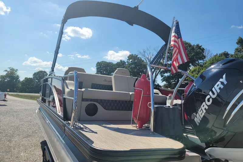 Slide: The Image of 2022 Barletta L23UC pontoon boat with Mercury engine and American flag, parked outdoors. - 11