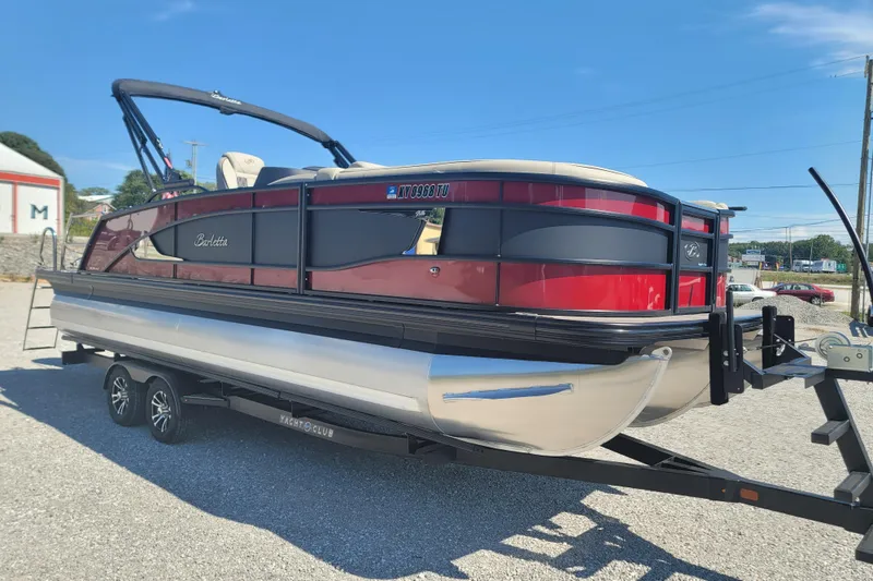 Slide: The Image of 2022 Barletta L23UC pontoon boat on trailer, red and black design, parked outdoors. - 17