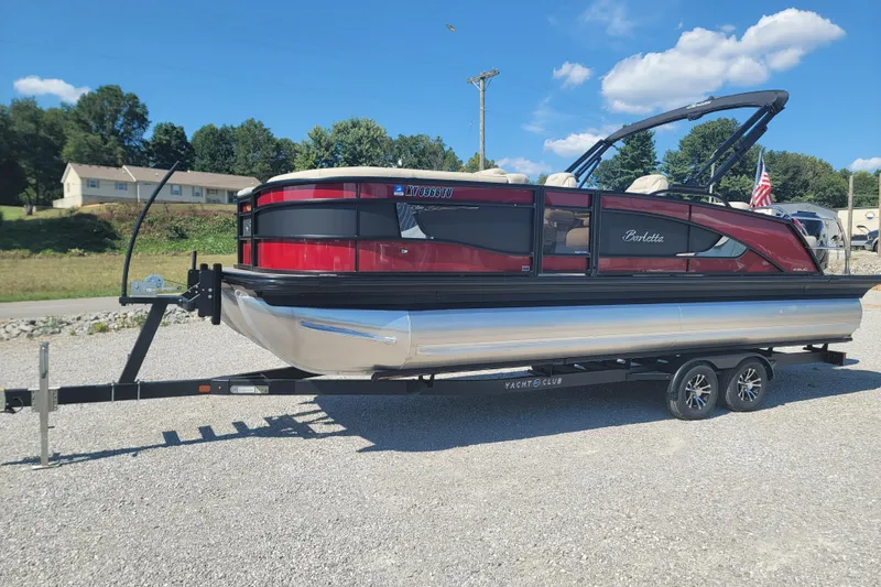 Slide: The Image of 2022 Barletta L23UC pontoon boat on trailer, red and black design, parked outdoors. - 2