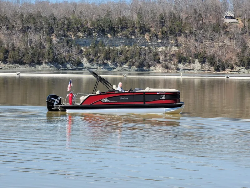 Slide: The Image of 2022 Barletta L23UC pontoon boat cruising on a calm lake with wooded shoreline. - 28