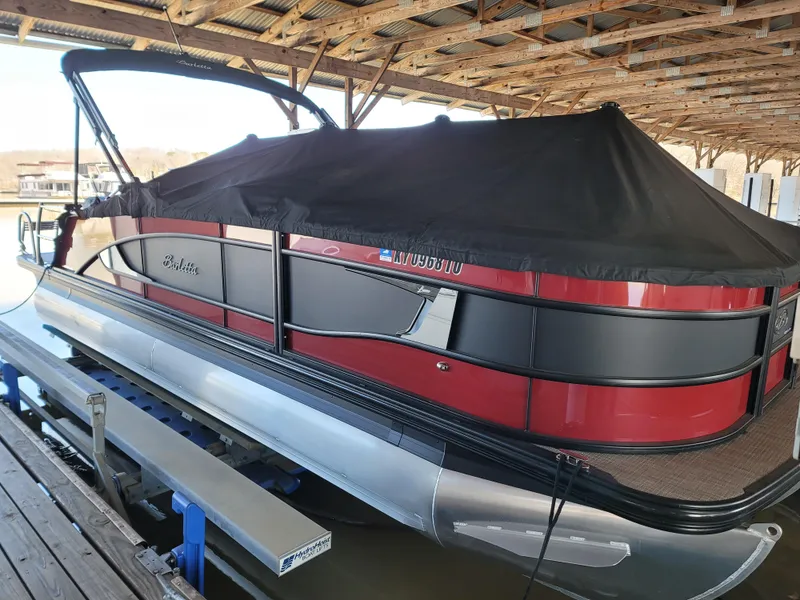 Slide: The Image of 2022 Barletta L23UC pontoon boat with black cover, docked under a wooden shelter. - 32