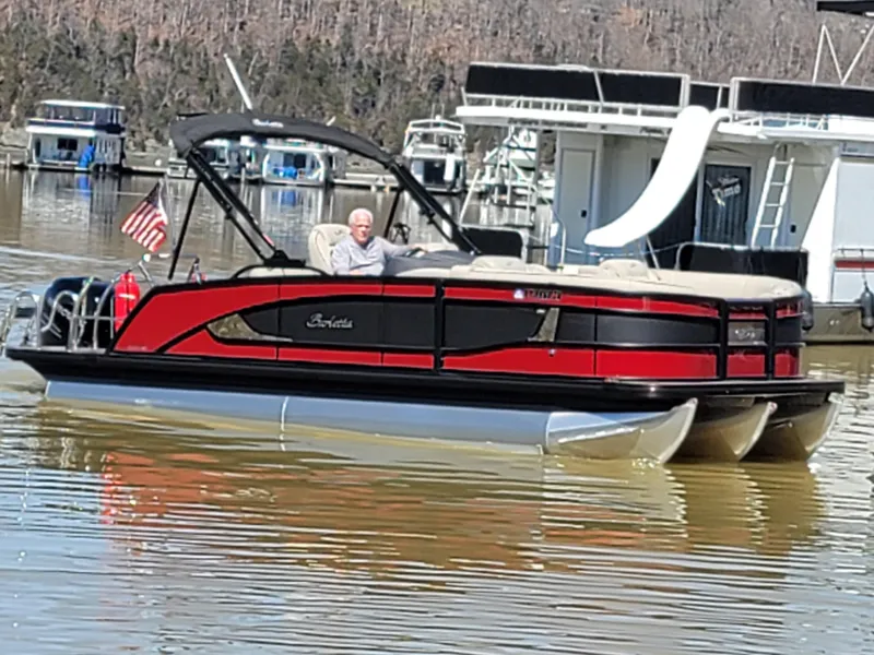 Slide: The Image of 2022 Barletta L23UC pontoon boat on a lake, featuring a red and black design. - 52