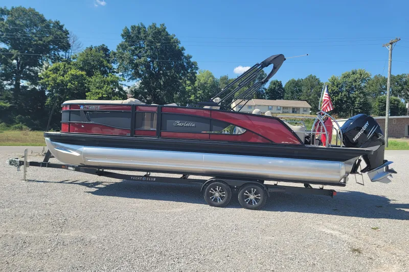 Slide: The Image of 2022 Barletta L23UC pontoon boat on trailer, parked outdoors, with trees in background. - 8