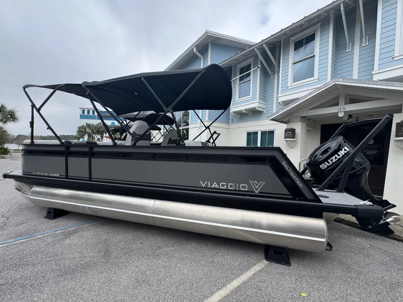 The Image of 2025 Viaggio Lago X-S pontoon boat with Suzuki engine, parked near a modern building. - 0