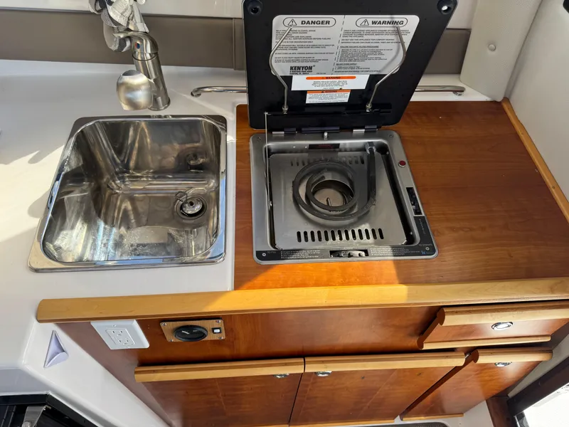 Slide: The Image of 2021 Cutwater C-24 Coupe kitchen with sink and stove, featuring wooden cabinetry. - 22