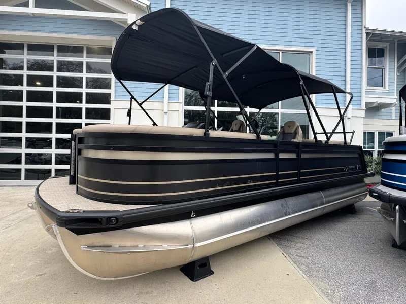 Slide: The Image of 2025 Viaggio Lago Z-U pontoon boat with black canopy, parked near a blue building. - 2