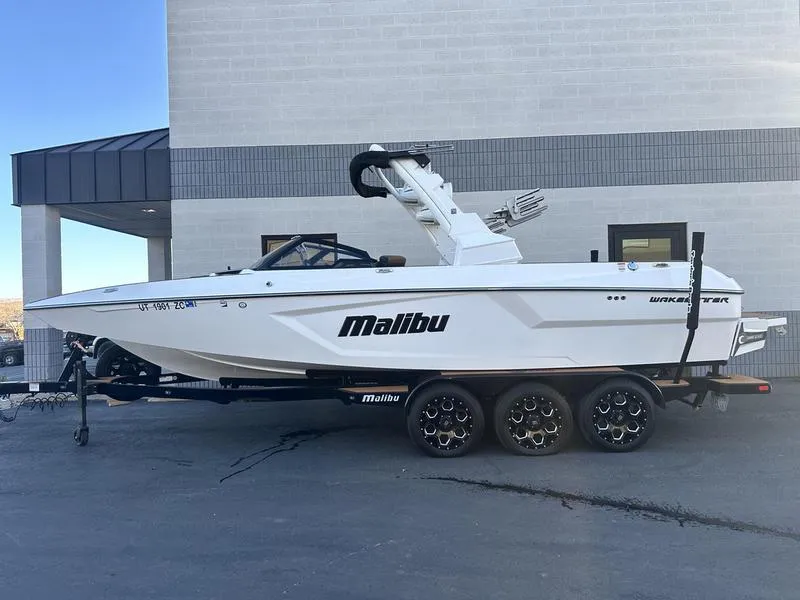 Slide: The Image of 2021 Malibu 24 MXZ boat on trailer, parked outside a building. - 0