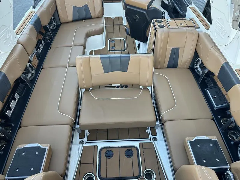 Slide: The Image of 2021 Malibu 24 MXZ boat interior with tan and black seating, cup holders, and storage compartments. - 17