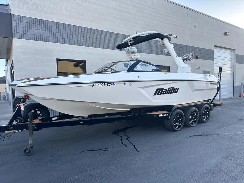 Slide: The Image of 2021 Malibu 24 MXZ boat on trailer, parked outside a building. - 2