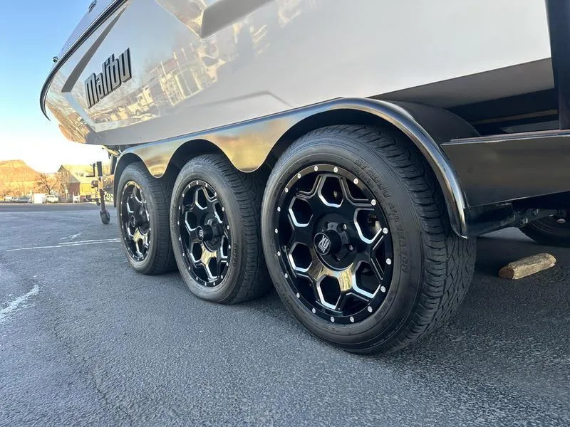 Slide: The Image of 2021 Malibu 24 MXZ boat trailer with stylish black wheels on pavement. - 4