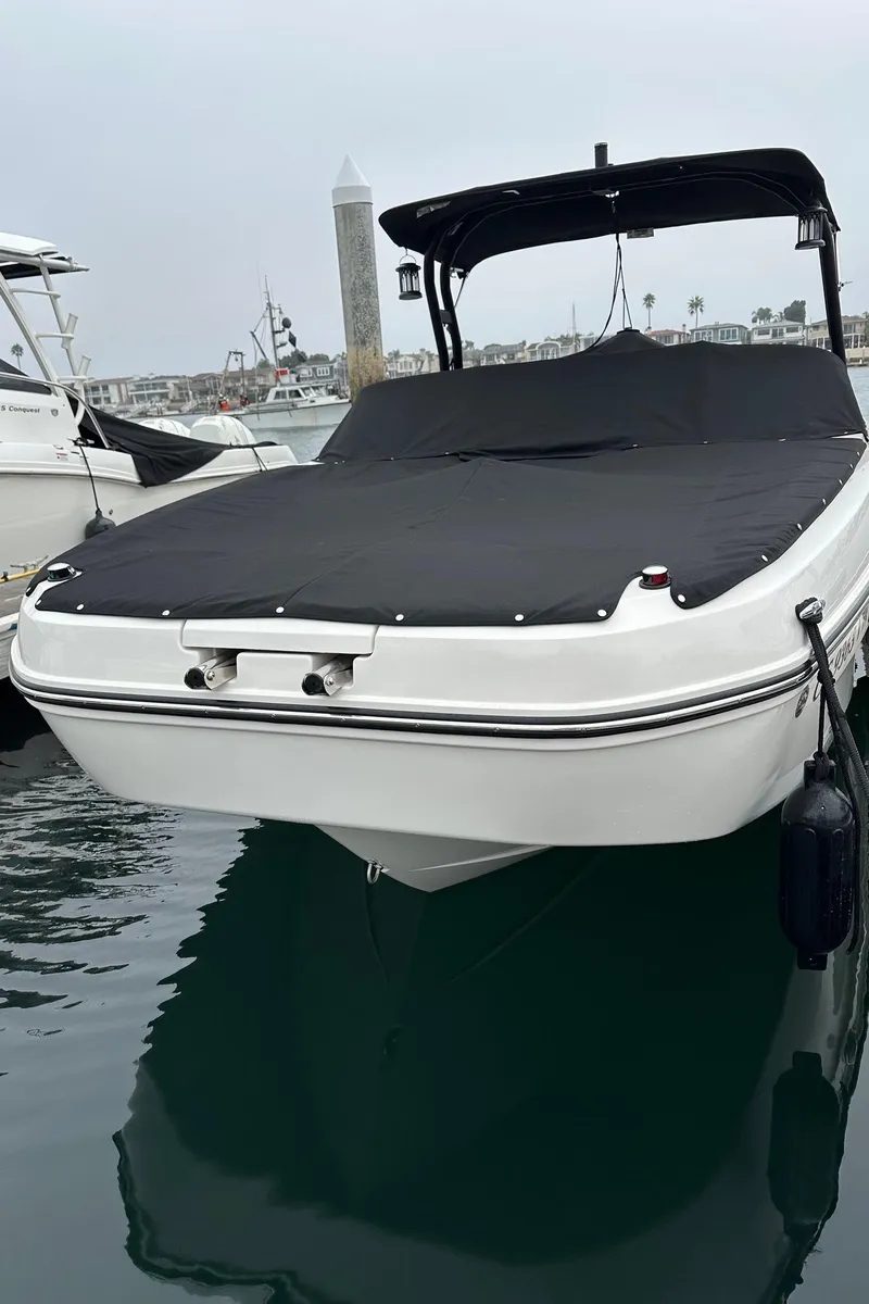 Slide: The Image of 2024 Bayliner DX 2250 boat docked with black cover, calm water background. - 10