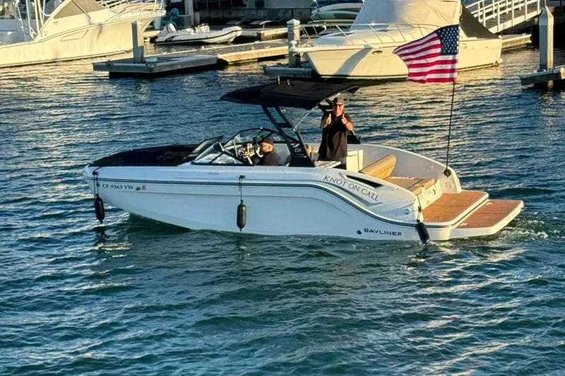 Slide: The Image of 2024 Bayliner DX 2250 boat cruising in marina with American flag. - 2