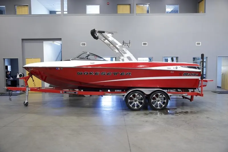 Slide: The Image of 2014 Malibu 247 LSV Wakesetter boat in a showroom, red and white design. - 0