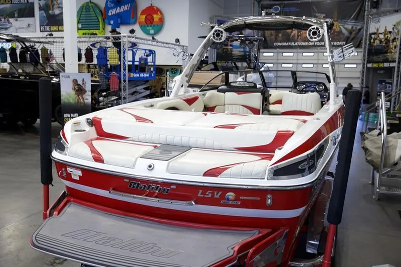 Slide: The Image of 2014 Malibu 247 LSV boat with red and white interior, displayed in a showroom. - 5