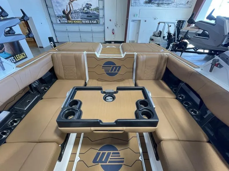 Slide: The Image of 2025 Malibu 23 MXZ boat interior with tan seating and central table in showroom. - 17