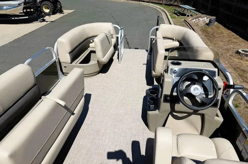Slide: The Image of 2025 Sun Tracker Party Barge 16 DLX interior with beige seating and steering console. - 2