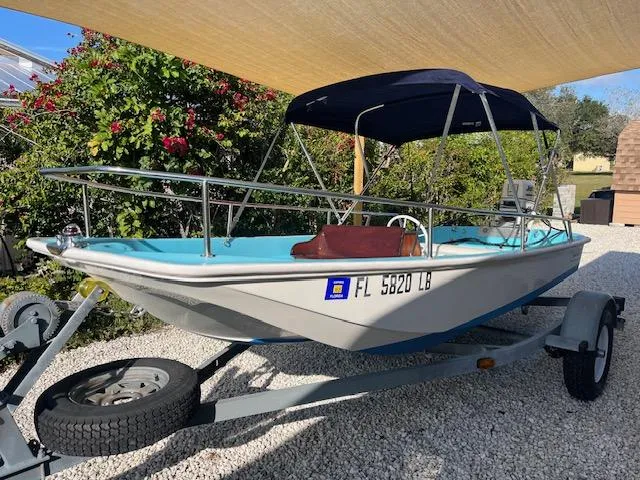 Slide: The Image of 1998 Boston Whaler 13 Sport boat on trailer, under canopy, with lush greenery background. - 44