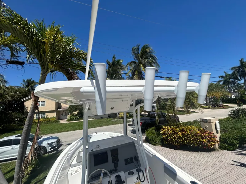 Slide: The Image of 2023 Release 210 RX boat with T-top and rod holders, parked near palm trees. - 28