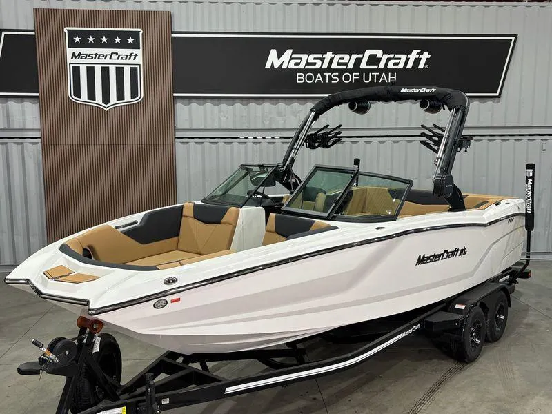The Image of 2025 MasterCraft NXT24 boat in showroom, white exterior, tan interior, displayed at MasterCraft Boats of Utah. - 1