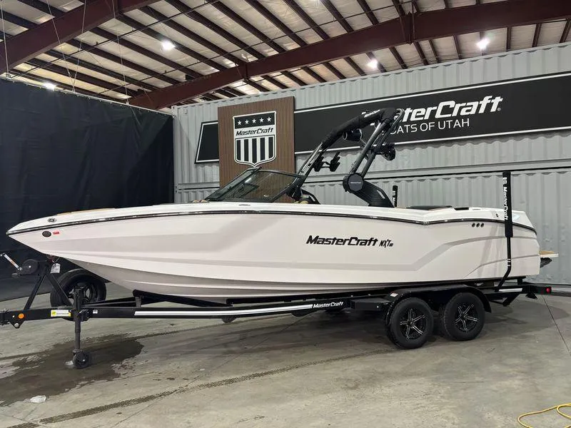 Slide: The Image of 2025 MasterCraft NXT24 boat in showroom, white exterior, on trailer. - 2