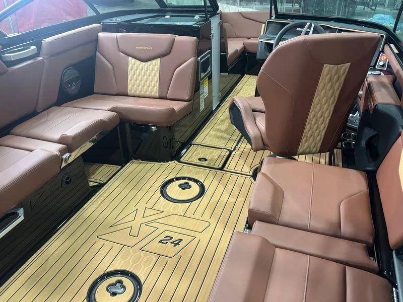 Slide: The Image of 2025 MasterCraft XT24 boat interior with brown leather seats and wood flooring. - 12