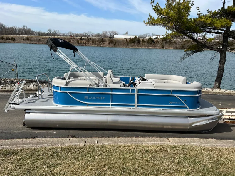 Slide: The Image of 2025 Godfrey Xperience Split Bench pontoon boat docked by a serene lake. - 3