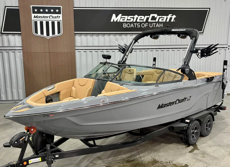 The Image of 2025 MasterCraft XT23 boat in showroom, gray exterior, tan interior, on trailer. - 1