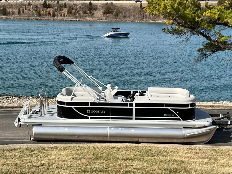 Slide: The Image of 2025 Godfrey Xperience Split Bench pontoon boat by a serene lake. - 1
