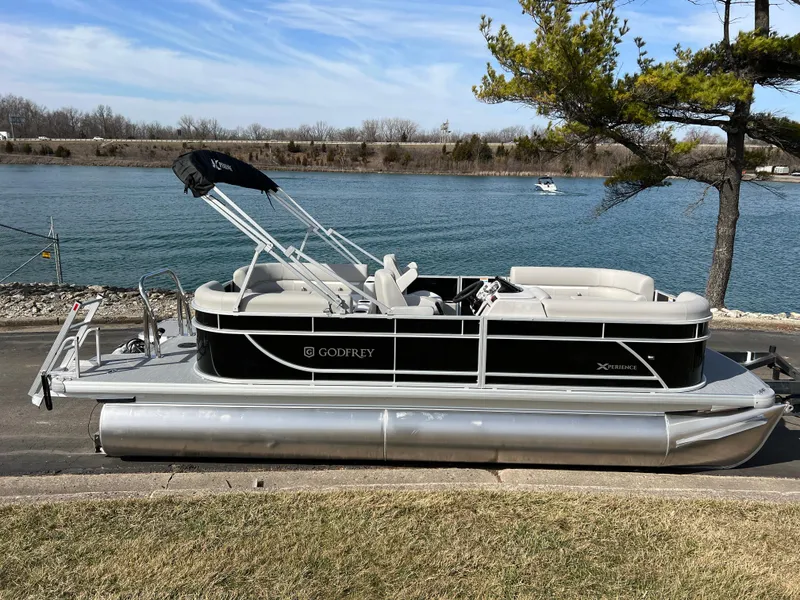 Slide: The Image of 2025 Godfrey Xperience Split Bench pontoon boat by a serene lake. - 3