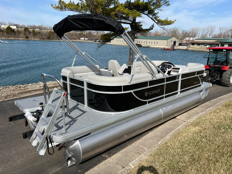 Slide: The Image of 2025 Godfrey Xperience Split Bench pontoon boat docked by a scenic lake. - 4