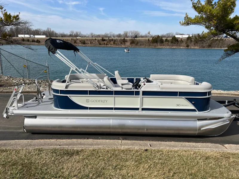 Slide: The Image of 2025 Godfrey Xperience Split Bench pontoon boat by a serene lake. - 3