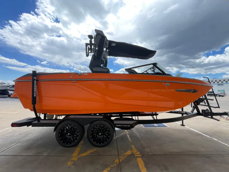Slide: The Image of 2023 Nautique Super Air Nautique G21 boat in vibrant orange on a trailer, under a cloudy sky. - 6