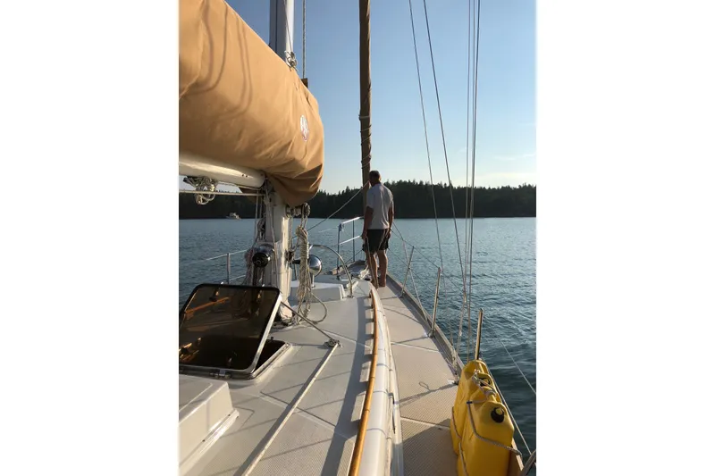 Slide: The Image of Man standing on 1986 Mason 33 sailboat deck, overlooking calm water and forested shoreline. - 17