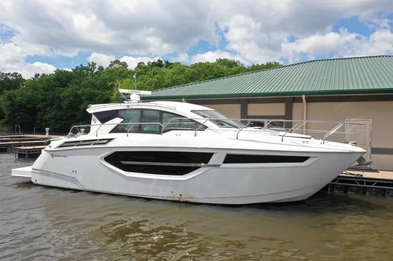 Slide: The Image of 2019 Cruisers Yachts 42 Cantius docked by a green-roofed building, under a partly cloudy sky. - 2