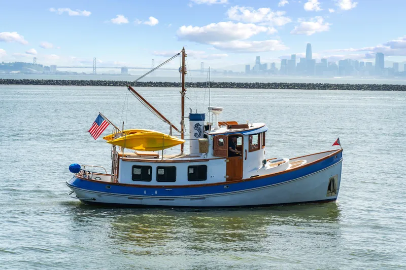 Slide: The Image of 1987 Lord Nelson 37 Victory Tug boat on calm water with city skyline in background. - 0