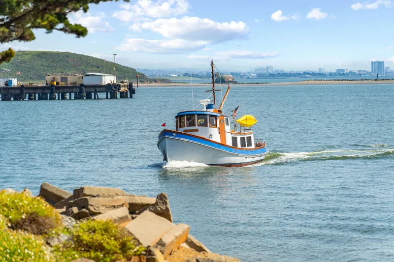 Slide: The Image of 1987 Lord Nelson 37 Victory Tug cruising near a rocky shoreline on a sunny day. - 27
