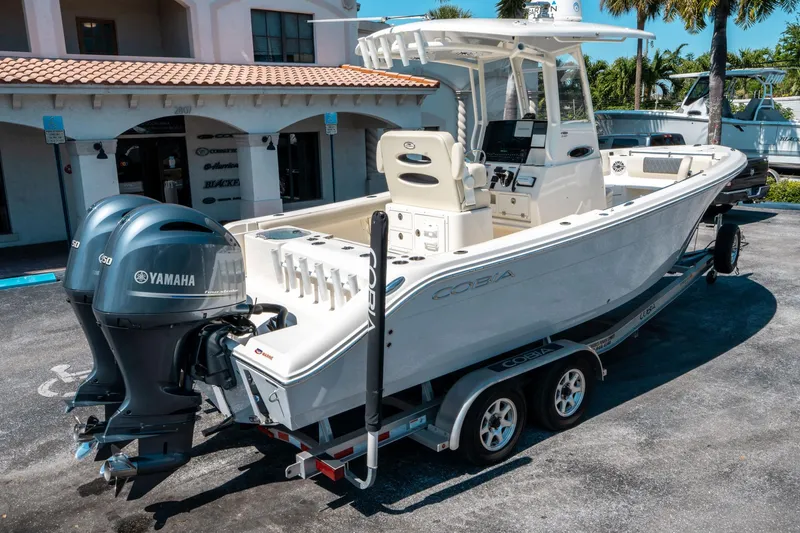 Slide: The Image of 2023 Cobia 240 CC boat with Yamaha engines on a trailer, parked outdoors. - 2