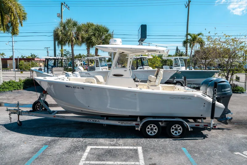 Slide: The Image of 2023 Cobia 240 CC boat on trailer, parked outdoors under clear blue sky. - 5