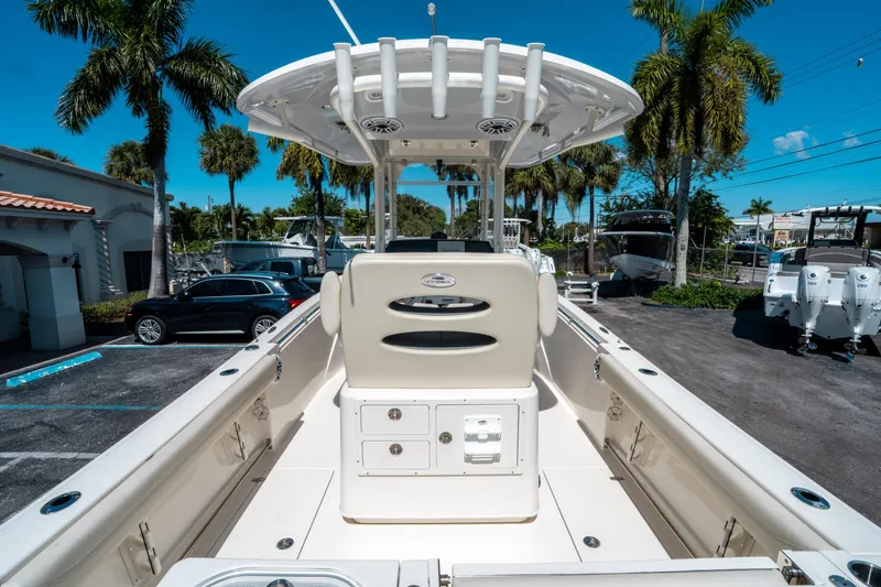 Slide: The Image of 2023 Cobia 240 CC boat interior with seating, palm trees, and parked cars in the background. - 9