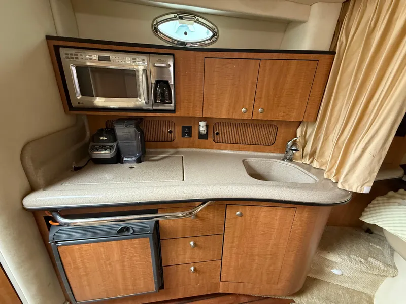 Slide: The Image of 2006 Sea Ray 320 Sundancer galley with microwave, sink, and wooden cabinetry. - 22