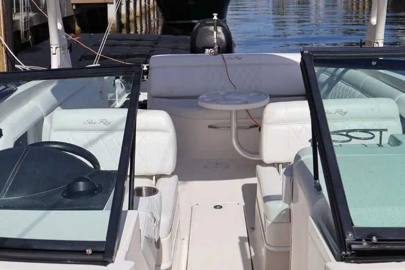 Slide: The Image of 2015 Sea Ray 270 Sundeck Outboard interior with white seating and table, docked by water. - 18