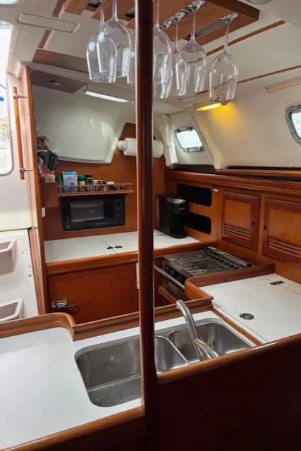 Slide: The Image of 2001 Beneteau 361 yacht kitchen with wood cabinetry, double sink, stove, and hanging glassware. - 19