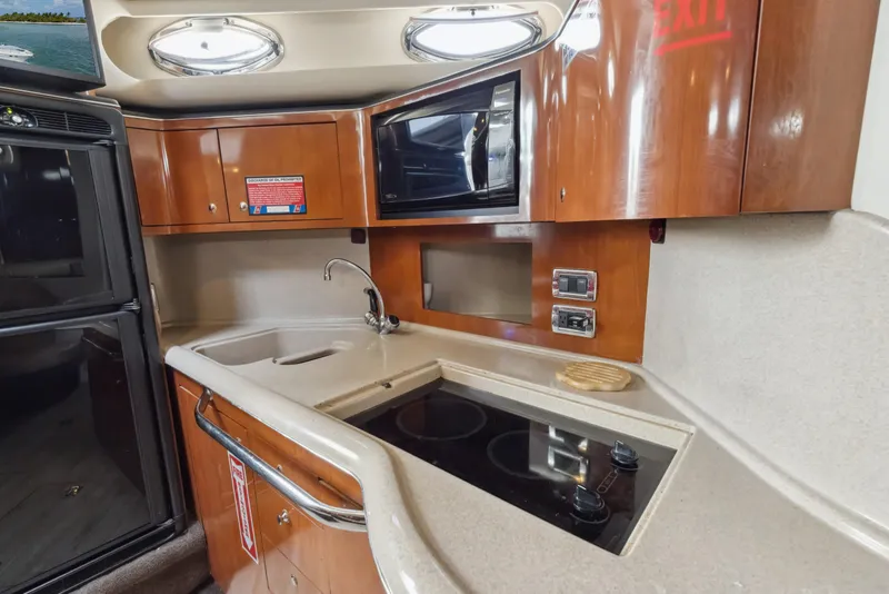 Slide: The Image of 2003 Sea Ray 380 Sundancer kitchen with stove, sink, microwave, and wooden cabinetry. - 18