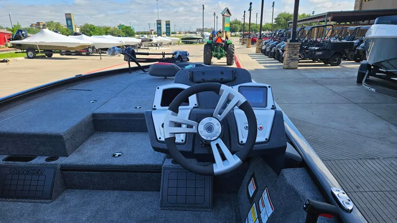 Slide: The Image of 2025 Tracker Savage 215 boat dashboard with steering wheel, parked outdoors. - 2