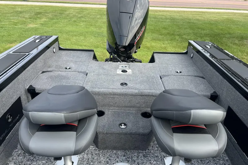 Slide: The Image of 2025 Tracker Targa V-18 Combo boat interior with two seats and motor, on grass. - 5