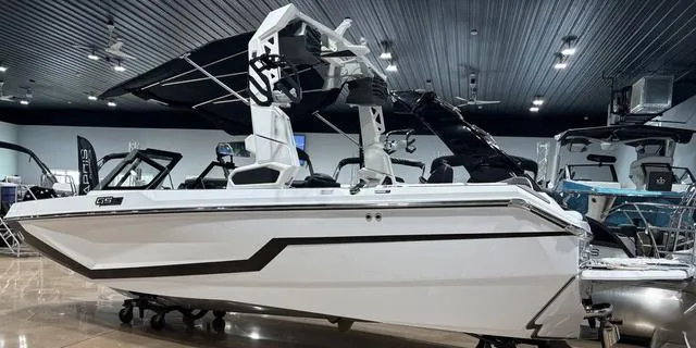 Slide: The Image of 2025 Nautique Super Air Nautique GS20 boat in showroom, sleek white design. - 2