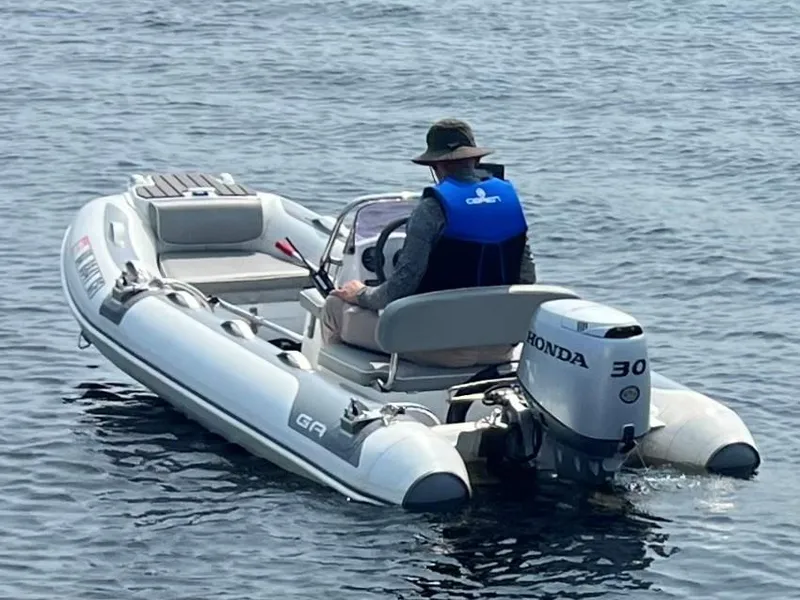 Slide: The Image of Man in a small inflatable boat with Honda motor on calm water. - 5