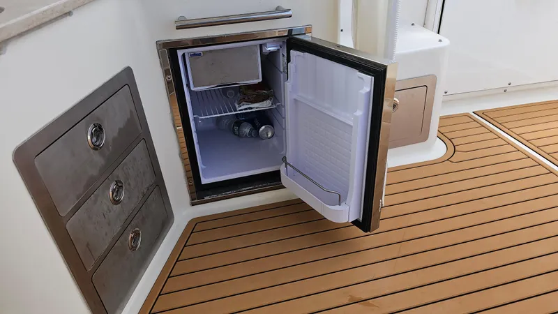 Slide: The Image of Open mini fridge on 2019 Sailfish 325 DC boat with wooden deck flooring. - 48