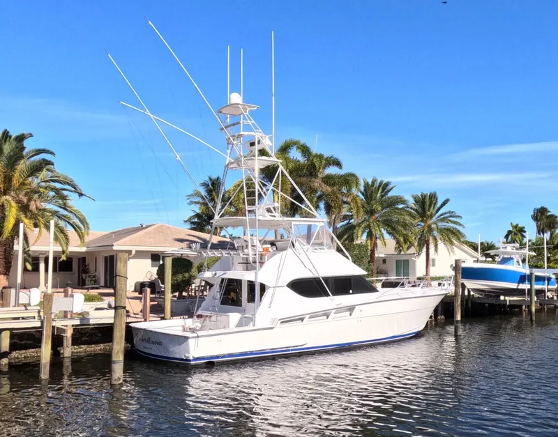 The Image of 2001 Hatteras 55 Convertible yacht docked by palm trees under clear blue sky. - 0
